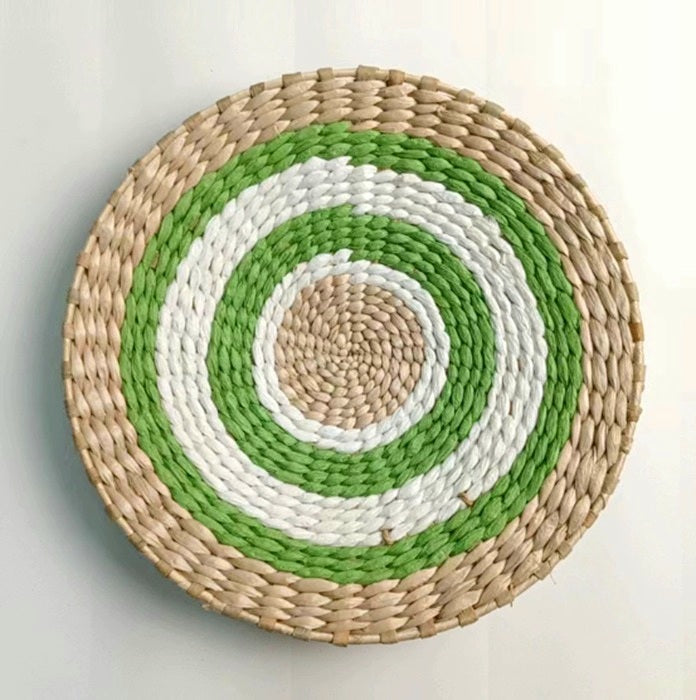 Round woven wall plate with concentric circles in green, white, and beige