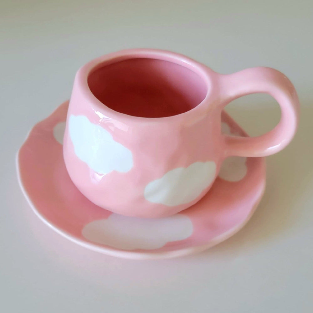 Pink ceramic cup with white cloud designs on a matching saucer 