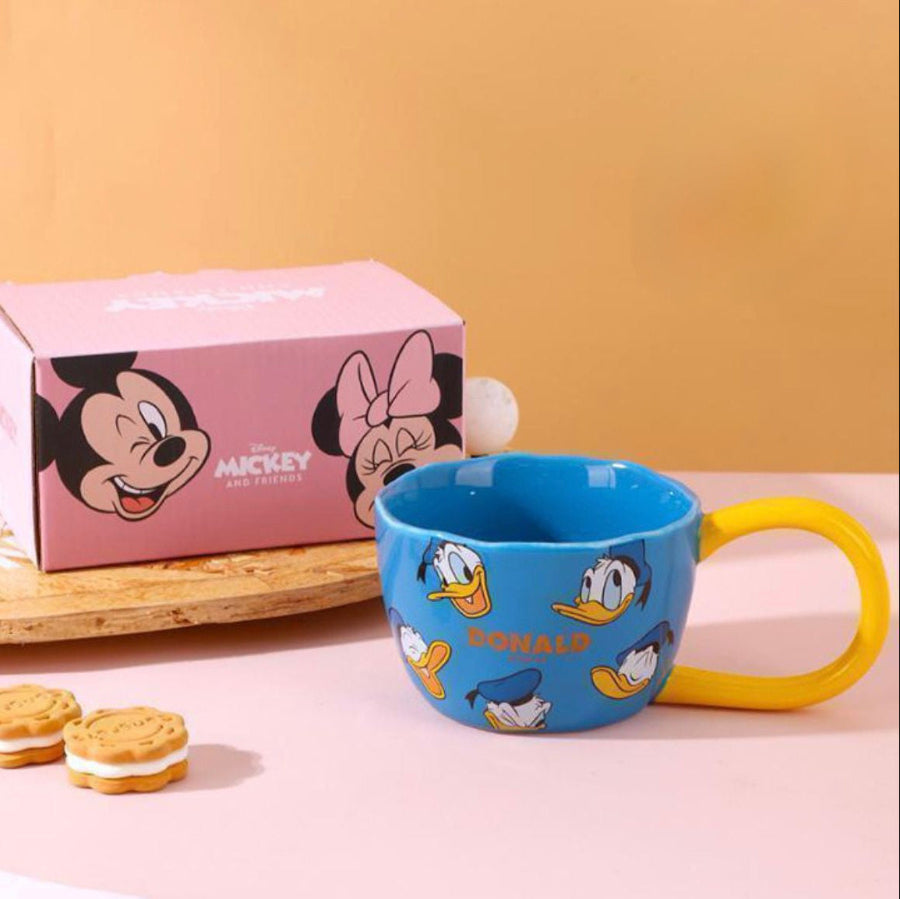 Blue mug with cartoon characters next to a pink box on a wooden surface.
