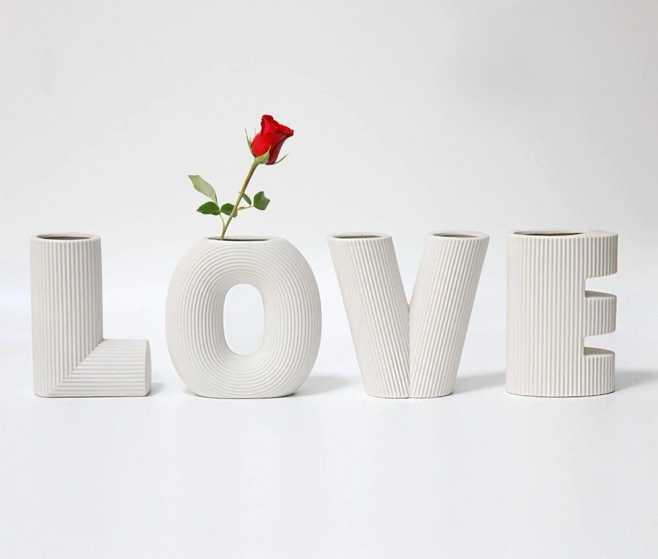 White letter-shaped vases spelling 'LOVE' with a red rose on a white background