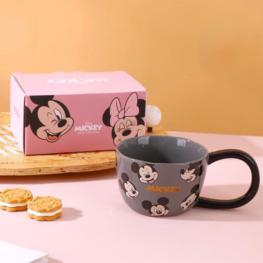 Gray mug with Mickey Mouse design next to a pink gift box on a pink surface.