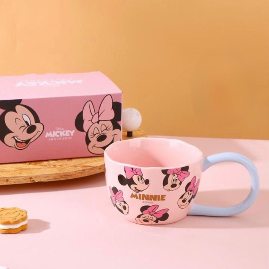 Pink mug with Minnie Mouse design next to a pink box with Minnie Mouse faces on a yellow background